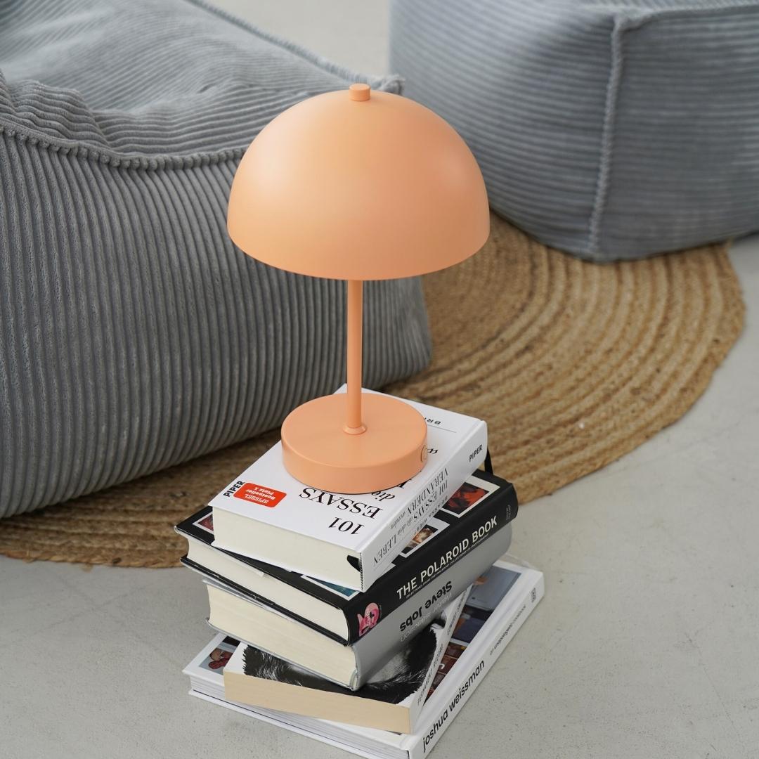 Lampe LED sans fil en pêche posée sur une pile de livres.