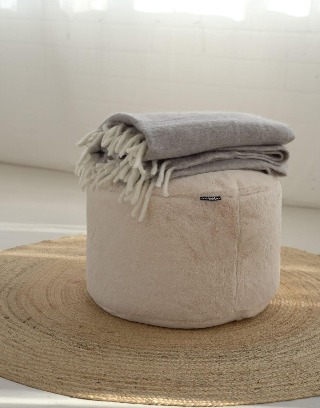 Pouf rond avec fausse fourrure douce en crème et un plaid gris dessus.